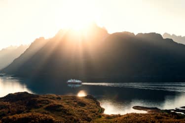 HX Hurtigruten Expeditions fartyg på havet i solnedgången mellan höga berg