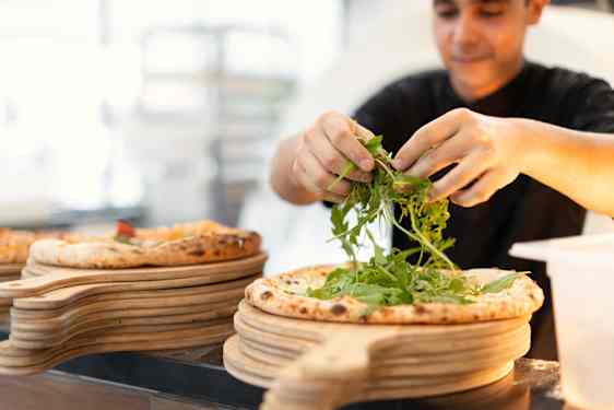 Man putting ruccola on pizza