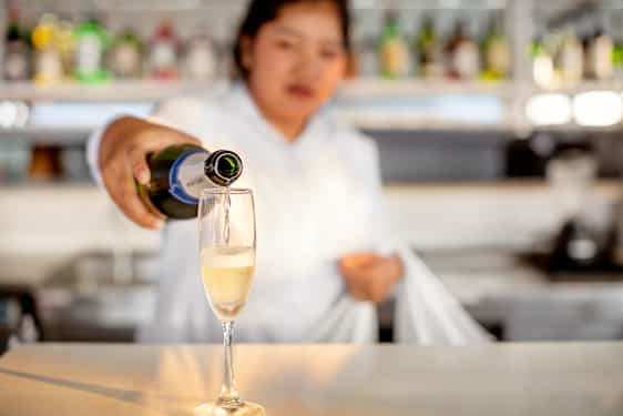 Waitress pouring sparkling wine into glass at bar