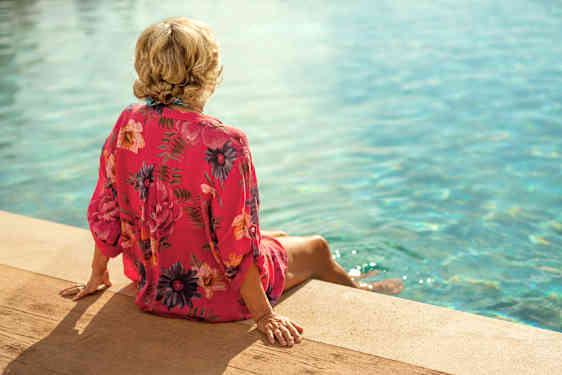Kvinna sitter vid en pool och doppar fötterna