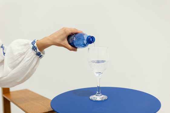 hand pouring water into glass on blue table