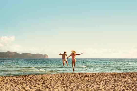 Couple holding hands and jumping in water at beach