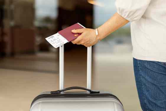 Woman holdin passport and ticket and drags suitecase