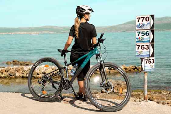 Woman leaning on bike by the sea looking at roadsigns